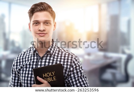 Young man holding a Bible in a modern office (concept for a successful businessman who has principles from the Holy Bible)
