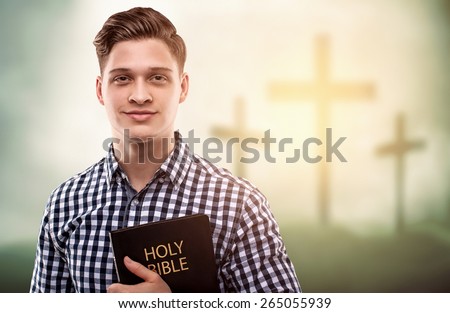 Young handsome happy man holding a Bible with tree crosses background (easter concept)