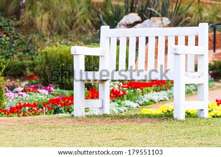 white wooden bench in garden among colorful flowers