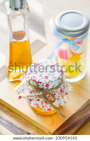 bottle of honey covered by vintage fabric and jelly bottle behind