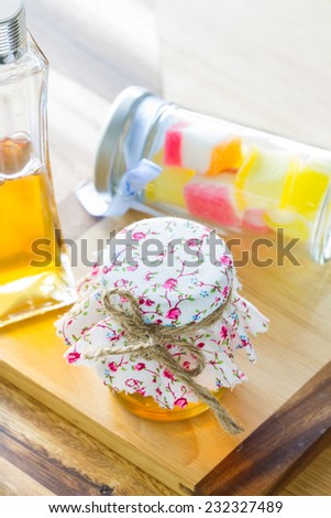 bottle of honey covered by vintage fabric and jelly bottle behind