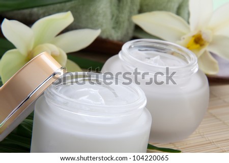 White Cymbidium orchid flower and jar of moisturizing face cream for spa treatment.