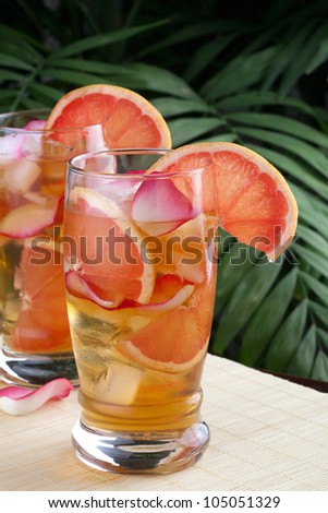 Two glasses of grapefruit and rose iced tea on a table in a restaurant on a tropical beach.