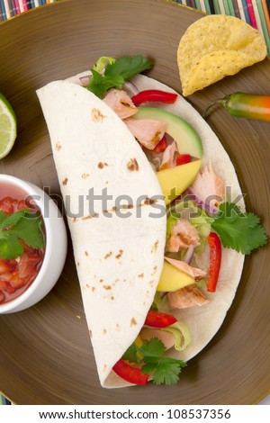 Closeup of grilled salmon fish tacos served with guacamole, fresh tomatoes salsa, and tortilla chips.