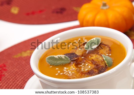 Closeup of a cup of hot delicious spicy roasted pumpkin soup with pumpkin crisps, sage and sesame seads.