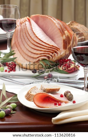 Closeup of plate with ham , bread and olives on dinning table set with glazed whole baked sliced ham, garnished with pomegranate.