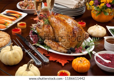 Roasted pepper turkey for Thanksgiving, garnished with pink pepper, blackberry, and fresh rosemary twigs on a dinner table decorated with mini pumpkins, beans, candles, and flutes of champagne.