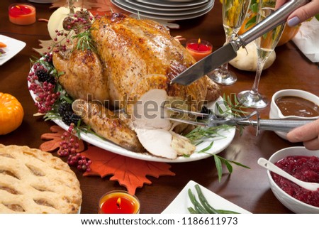 Carving roasted pepper turkey for Thanksgiving, garnished with pink pepper, blackberry, and fresh rosemary twigs on a dinner table decorated with mini pumpkins, beans, carrots, candles
