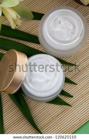 White Cymbidium orchid flower and jar of moisturizing face cream for spa treatment.