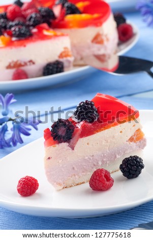 Piece of fruit yogurt cake. Cream and yogurt based fruit filling topped with jelly. Raspberries, blackberries, stawberries, and oranges.