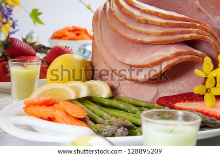 Table set with festive glazed ham for Easter celebration dinner garnished with asparagus, carrots, strawberry, and lemon wedges.