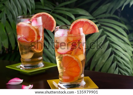 Two glasses of grapefruit and rose iced tea on a table in a restaurant on a tropical beach.