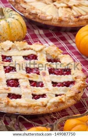 Cherry pie with lattice top on fall themed napkin, and mini pumpkins.