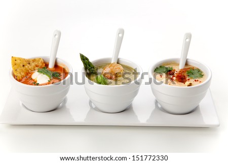 Closeup of three bowls of vegetable Tortilla-Chipotle soup, Cream of Asparagus soup, and Chilled Corn and Bacon soup over white background