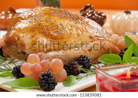 Rosemary-basil rub roasted turkey breast garnished with grapes, blackberies, and fresh basil, and rosemary in fall themed surrounding.
