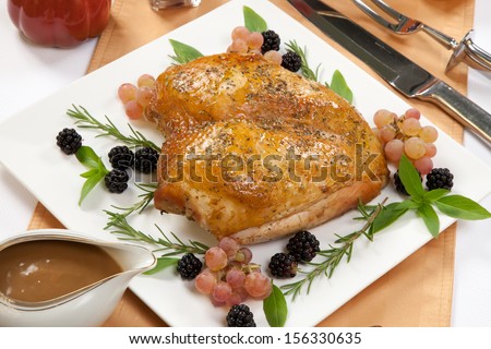 Rosemary-basil rub roasted turkey breast garnished with grapes, blackberies, and fresh basil, and rosemary in fall themed surrounding.