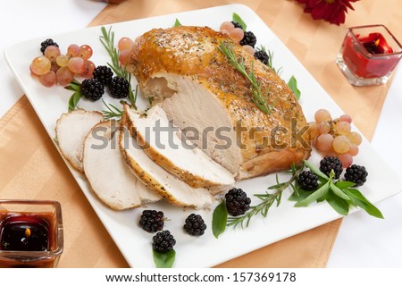 Carved Rosemary-Basil Rub Roasted Turkey Breast Garnished With Grapes, Blackberies, And Fresh Basil, And Rosemary In Fall Themed Surrounding.