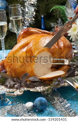 Carving roasted turkey garnished with herbs on blue Christmas decorations and champagne Christmas tree as background Carving roasted turkey garnished with herbs on blue Christmas decorations and champagne Christmas tree as background
