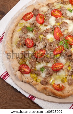 Leak, cherry tomato, and meat pizza on baking stone. Made with ground lamb. Home made. Garnished with parsley leafs.