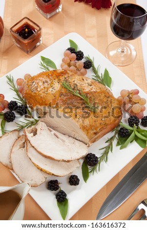Carved Rosemary-basil rub roasted turkey breast garnished with grapes, blackberies, and fresh basil, and rosemary in fall themed surrounding.