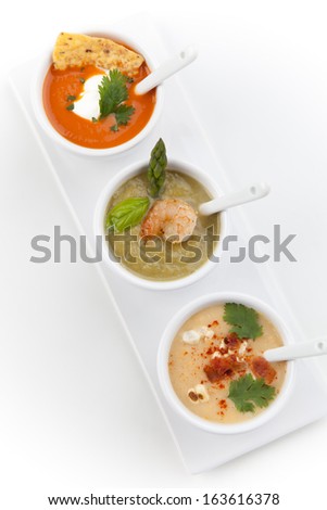 Closeup of three bowls of vegetable Tortilla-Chipotle soup, Cream of Asparagus soup, and Chilled Corn and Bacon soup over white background