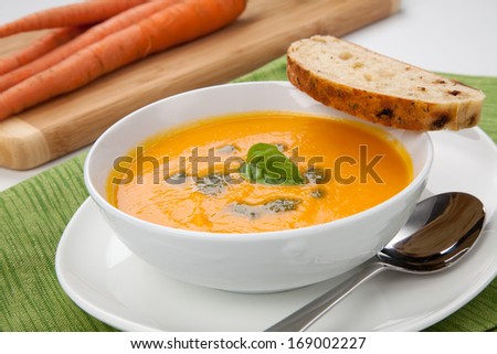 Creamy carrot soup with basil oil, garnished with herb whole wheat bread. Fresh carrots around.