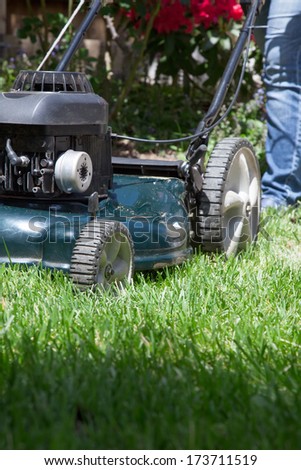 Woman is mowing her lawn with lawn mower in her back yard