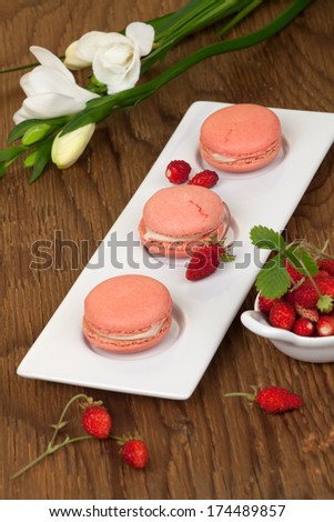 Closeup of a row of french strawberry macaroons with fresh alpine strawberries.