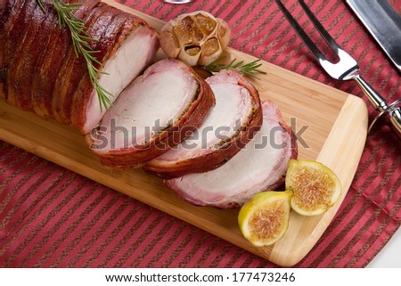 Closeup of delicious sliced roasted bacon - wrapped pork loin with roasted garlic, and fresh rosemary.