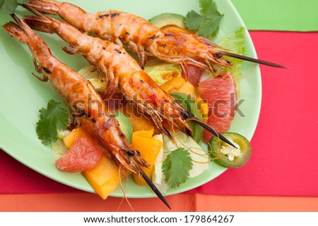 Close up of whole grilled large shrimps -scampi- on bamboo sticks served with spicy avocado-citrus salad.