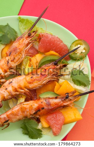 Close up of whole grilled large shrimps -scampi- on bamboo sticks served with spicy avocado-citrus salad.