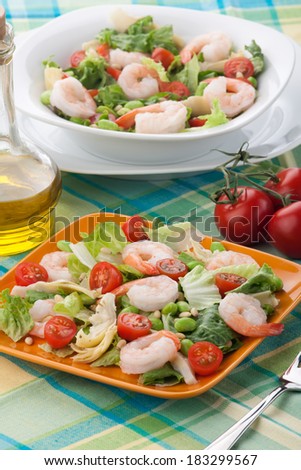 Two plates of Italian shrimp salad with shrimps, tomatoes, artishocke hearts, Romane lettuce leaves, fava beans, and pine nuts. Olive oil.