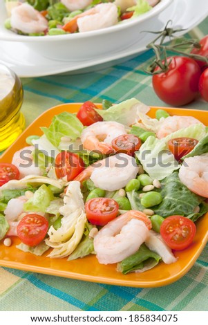 Two plates of Italian shrimp salad with shrimps, tomatoes, artishocke hearts, Romane lettuce leaves, fava beans, and pine nuts. Olive oil.