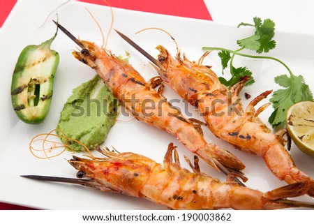 Close up of spicy whole grilled large shrimps -scampi- with guacamole sauce and grilled jalapeno pepper.