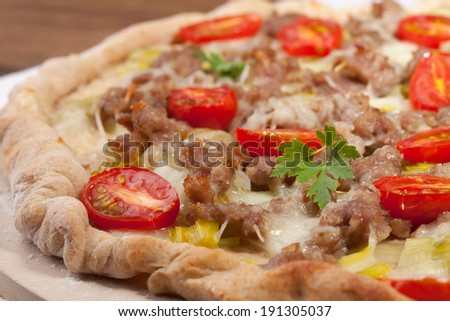 Leak, cherry tomato, and meat pizza on baking stone. Made with ground lamb. Home made. Garnished with parsley leafs.