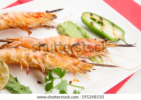 Close up of spicy whole grilled large shrimps -scampi- with guacamole sauce and grilled jalapeno pepper.