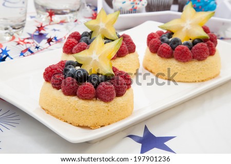 Tray of fresh Angel food fruit cakes with raspberry, blueberry, and star fruit. Muffins on 4th of July in patriotic theme in background.