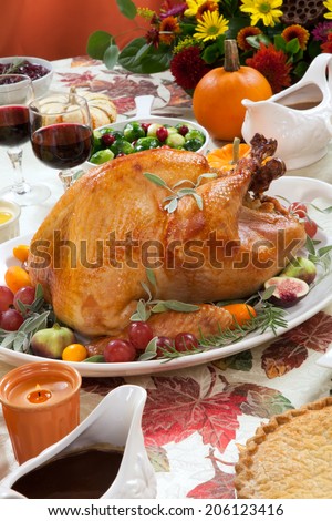 Roasted turkey on a server tray garnished with fresh figs, grape, kumquat, and herbs on fall harvest table. Red wine, side dishes, pie, and gravy. Decoraded with mini pumpkins, candels, and flowers.