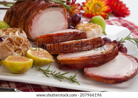 Closeup of delicious one piece roasted bacon - wrapped pork loin with roasted garlic, grapes, figs, and fresh rosemary.