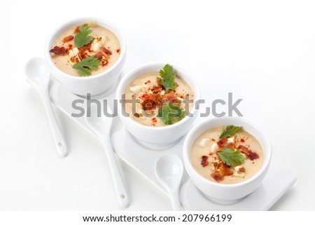 Three bowls of Chilled Corn and Bacon soup garnished with cooked bacon, fresh cilantro, and smoked paprika