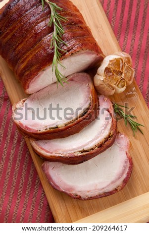 Closeup of delicious sliced roasted bacon - wrapped pork loin with roasted garlic, and fresh rosemary.