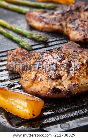 Juicy pork chops are grilled on griddle with asparagus and bell pepper. Backyard grilling for summer picnic.