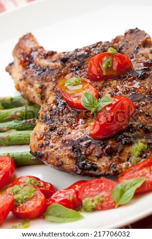 Grilled pork chops and asparagus. Served with fried grape tomatoes salad and pesto sauce.