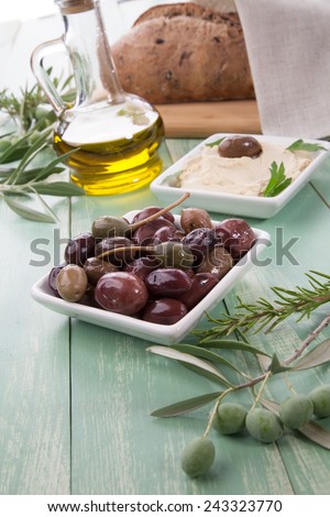 Greek style black olives, hummus, olive oil, and bread on a wooden table