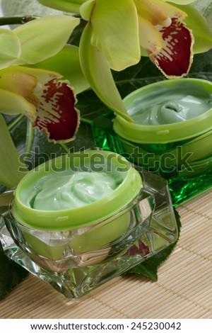 Closeup of two jars of cosmetics cream and blooming Cymbidium orchid flowers for everyday use.
