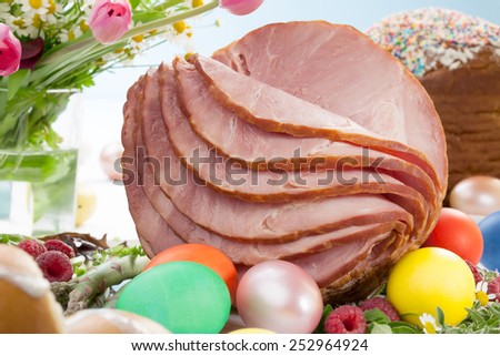 Whole baked honey sliced ham with fresh raspberry, asparagus, dyed Ester eggs, Easter cake, and cross buns. Spring flowers.