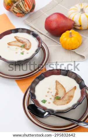 Two bowls of hot delicious Roasted Parsnip and Pear Soup. Garnished with slices of caramelized pears, maple syrup, and parsley. Pumpkins and bread.