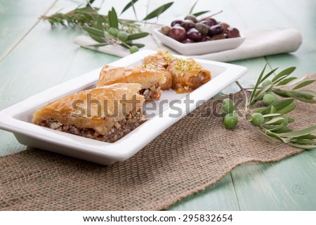 Mediterranean traditional pastries - Baklava - served with Greek style black olives on a wooden table
