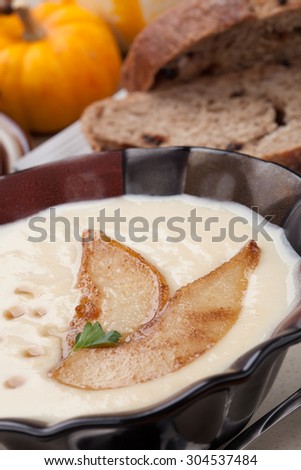 Two bowls of hot delicious Roasted Parsnip and Pear Soup. Garnished with slices of caramelized pears, maple syrup, and parsley. Pumpkins and bread.