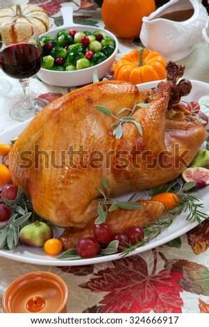 Roasted turkey on a server tray garnished with fresh figs, grape, kumquat, and herbs on fall harvest table. Red wine, side dishes, pie, and gravy. Decoraded with mini pumpkins, candels, and flowers.